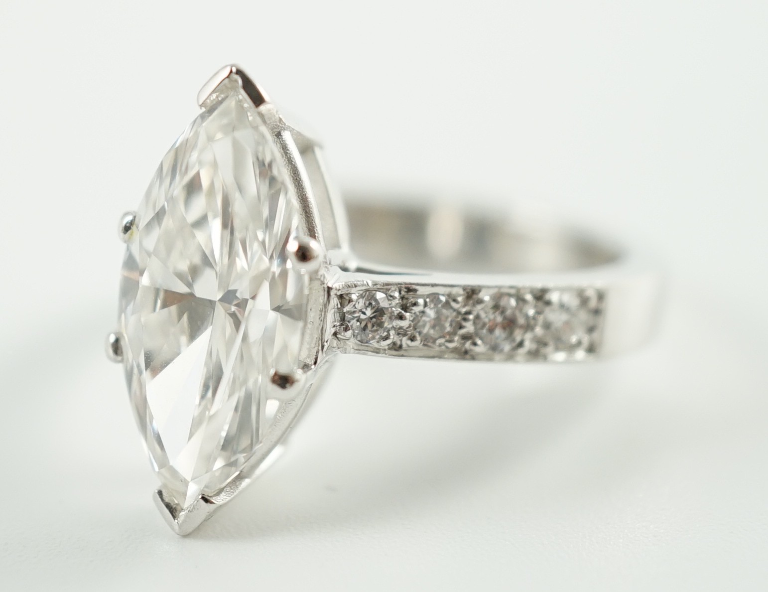 A modern 18ct white gold and single stone marquise diamond set dress ring, with graduated diamond set shoulders, with accompanying WGI report dated 18/6/2021, stating the stone to weigh 3.70ct